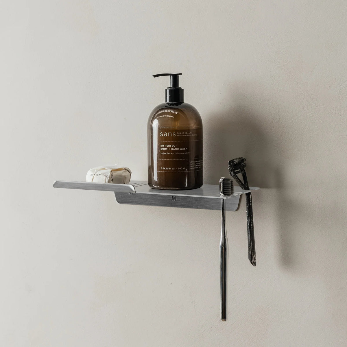 Brushed aluminium FOLD shower shelf holding an amber bottle, razor and toothbrush