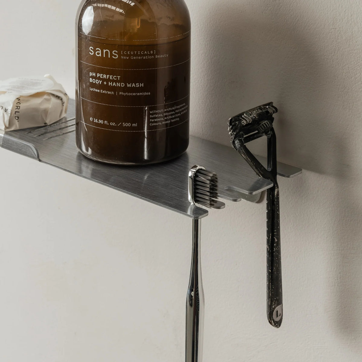 Close view of the brushed aluminium FOLD shower shelf with an amber bottle and razor