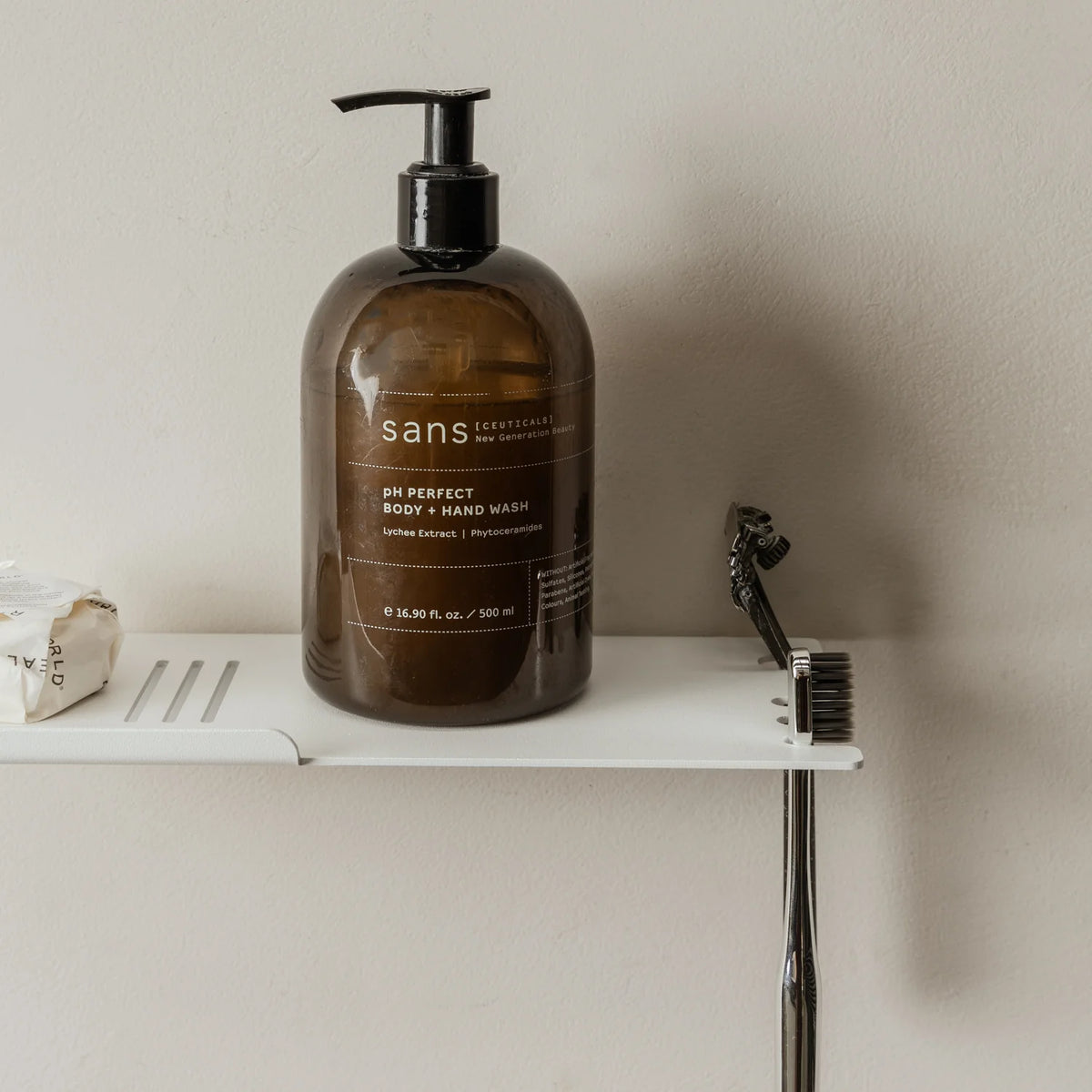 White FOLD shower shelf with an amber pump bottle and razor on a grey wall