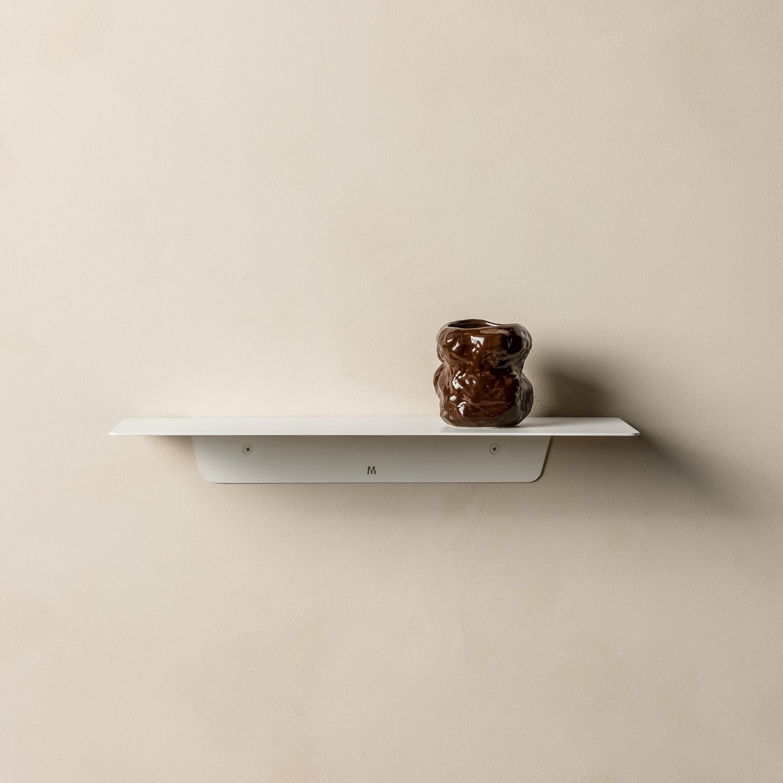 White FOLD Ledge holding a dark glazed ceramic vase against a beige wall