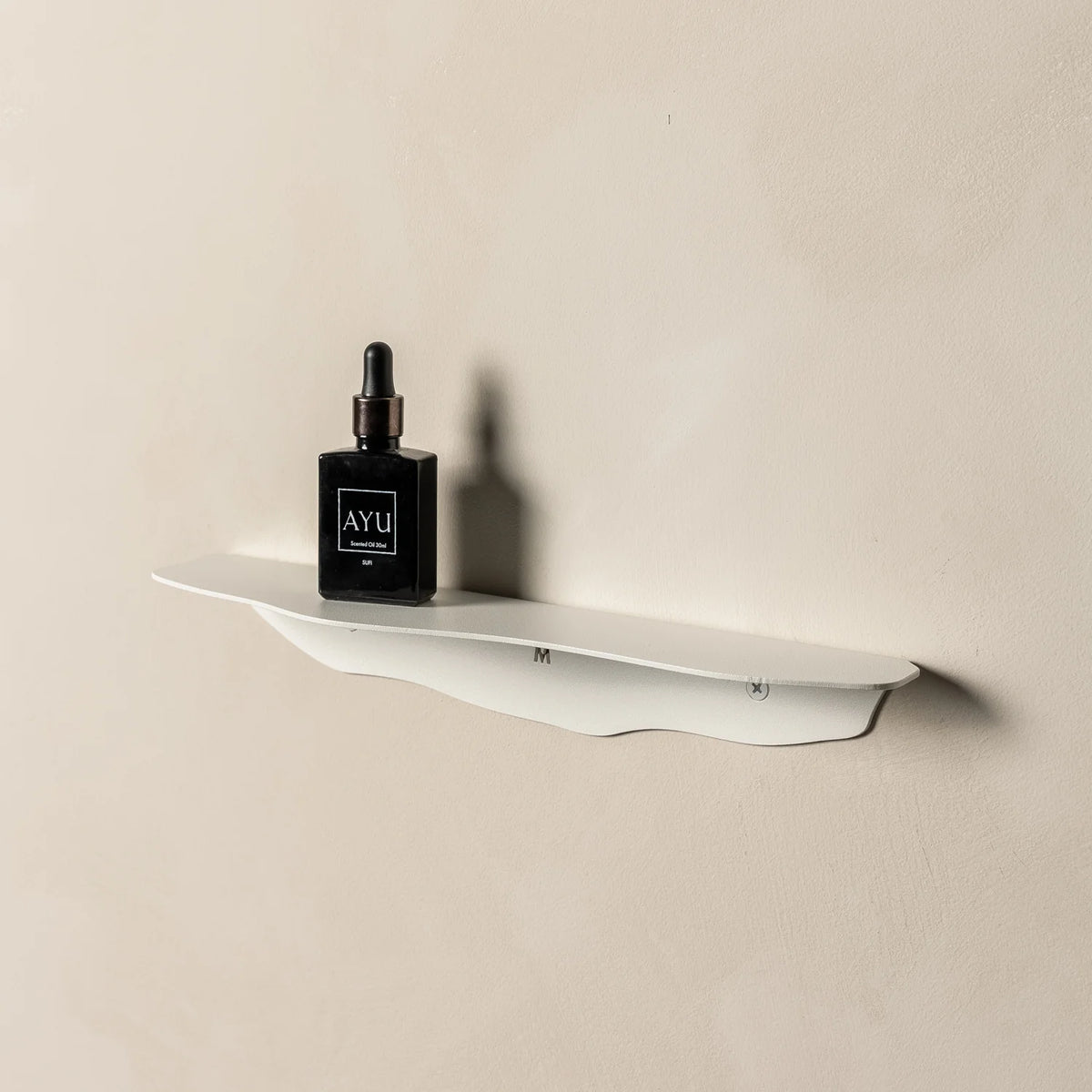 White wavy shelf on beige plaster seen from the left, holding the same small dark bottle