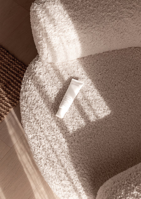 Small white hand cream tube lying on a boucle armchair seat in dappled sunlight