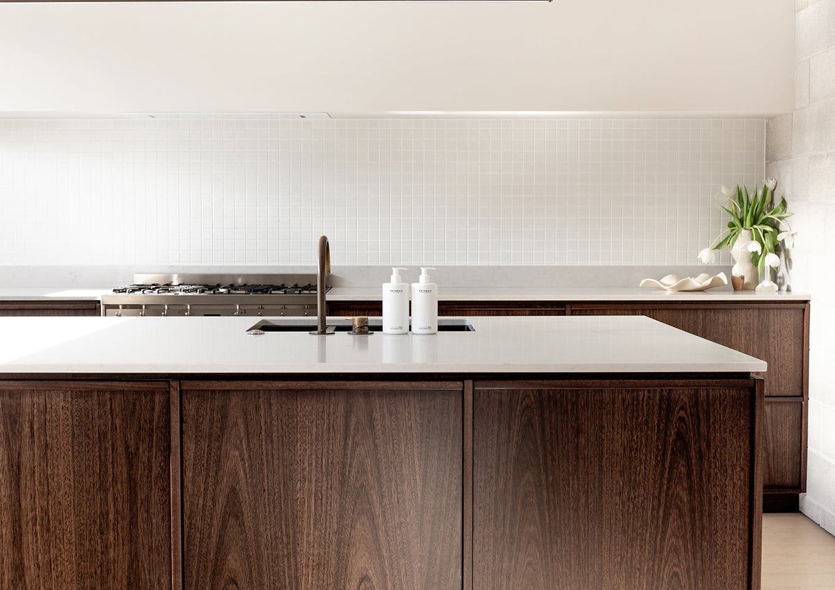 Landscape view of a dark timber kitchen island with two small bottles by the tap