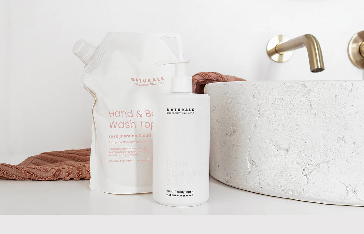 Naturals hand and body wash refill pouch beside a white pump bottle and a stone basin