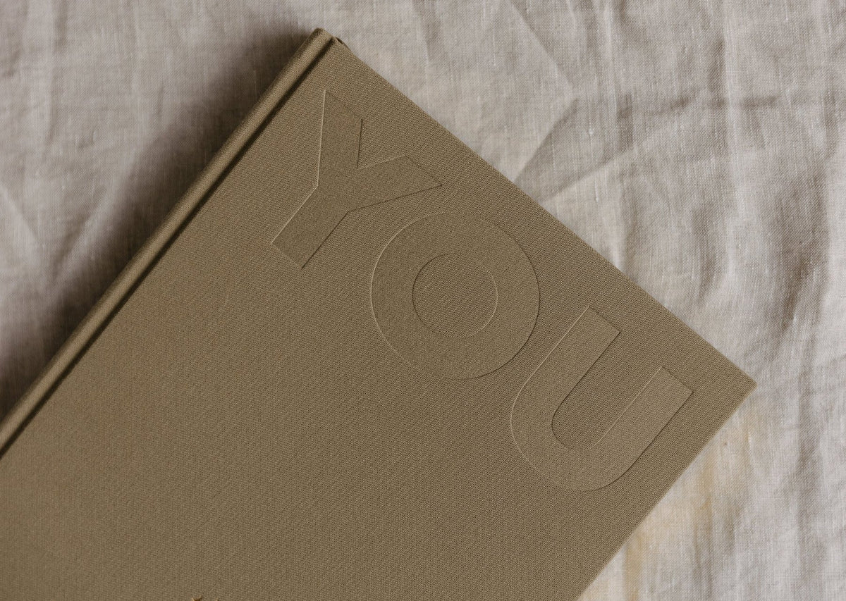 Close view of the sand YOU. journal on linen, showing the debossed YOU lettering on the cover