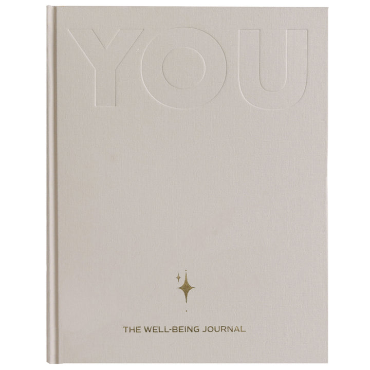 Front cover of the sand YOU. journal with debossed YOU lettering, a gold star motif and the words The Well-Being Journal