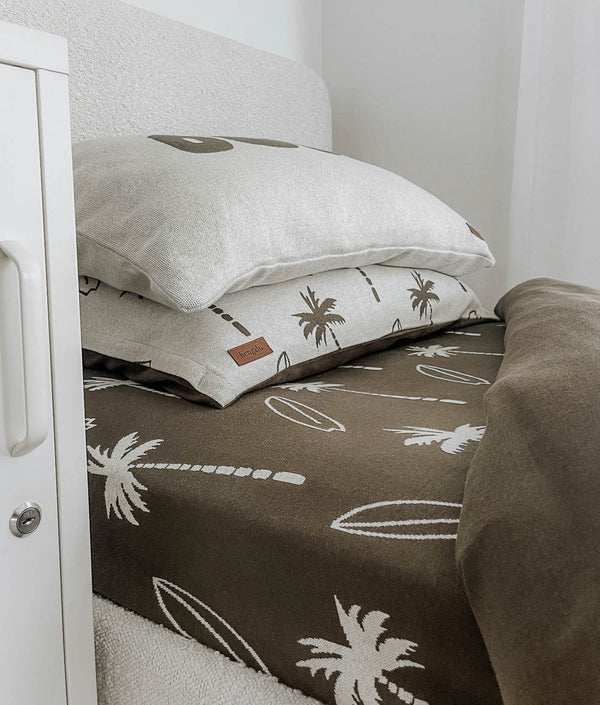 Surfing Palm kids cotton pillowcase under a plain pillow on an olive Surfing Palm jersey fitted sheet