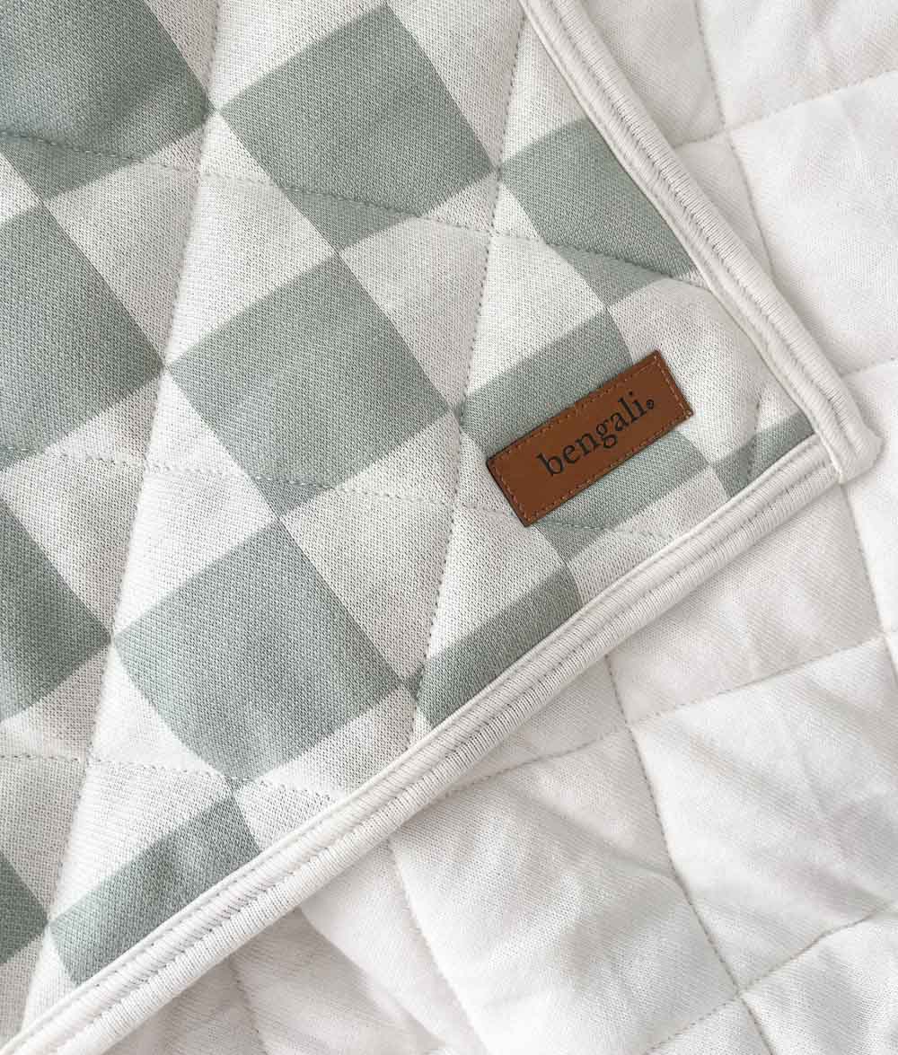 Corner of the Sage Gingham reversible quilt with leather Bengali label over its plain ivory side