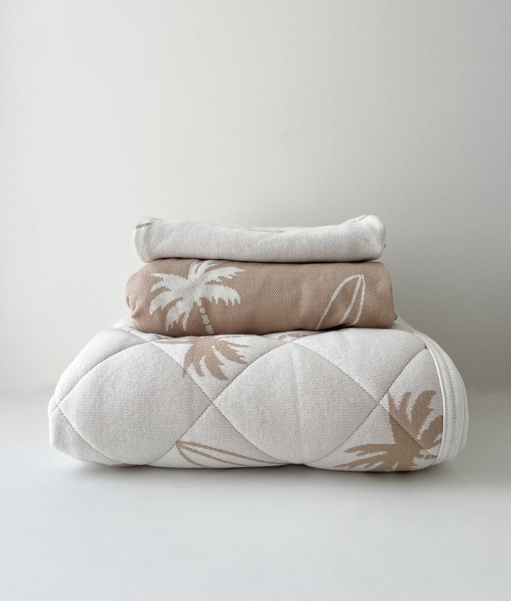 Folded Surfing Palm bedding on white: pillowcase, sand jersey fitted sheet and quilted Surfing Palm reversible quilt