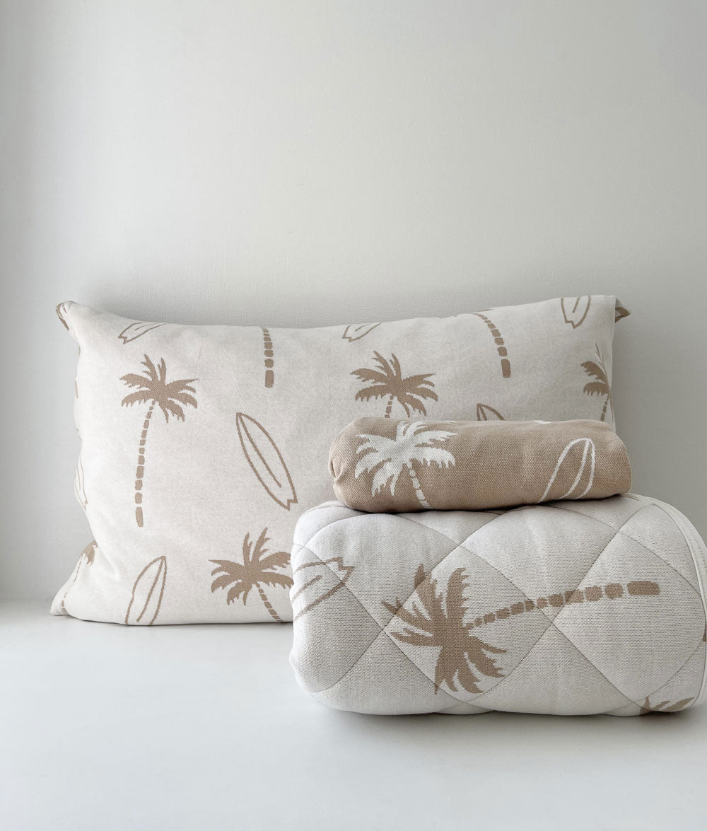 Rolled natural Surfing Palm reversible quilt with a folded sand fitted sheet and Surfing Palm pillowcase