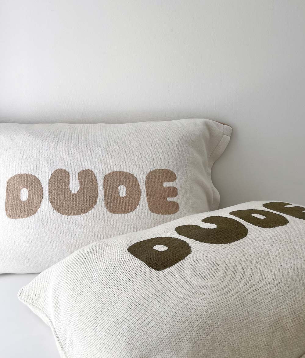 Two DUDE jersey cotton pillowcases, one with sand lettering and one with olive lettering, on white