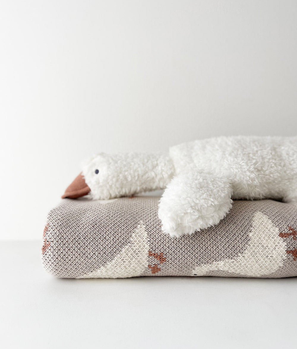 Gary the Goose ivory sherpa baby comforter resting on a folded goose print knit blanket