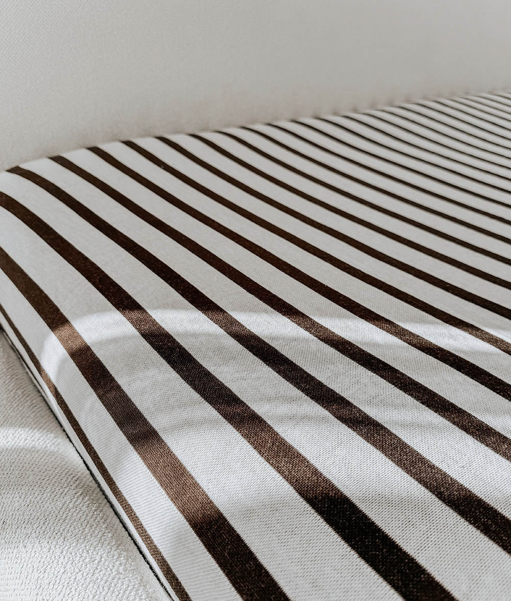 Chocolate and ivory striped jersey fitted sheet across a bed with an ivory textured throw at the foot