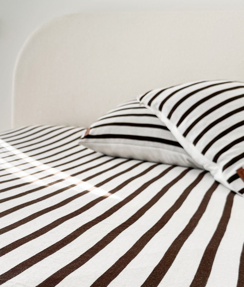 Striped chocolate and ivory pillow on the Sundown Stripe fitted sheet against a curved ivory headboard
