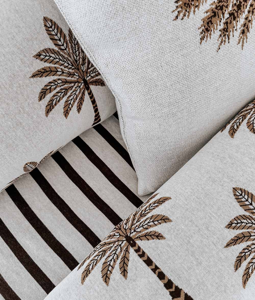 Close-up of palm print cushions layered against the chocolate and ivory Sundown Stripe sheet