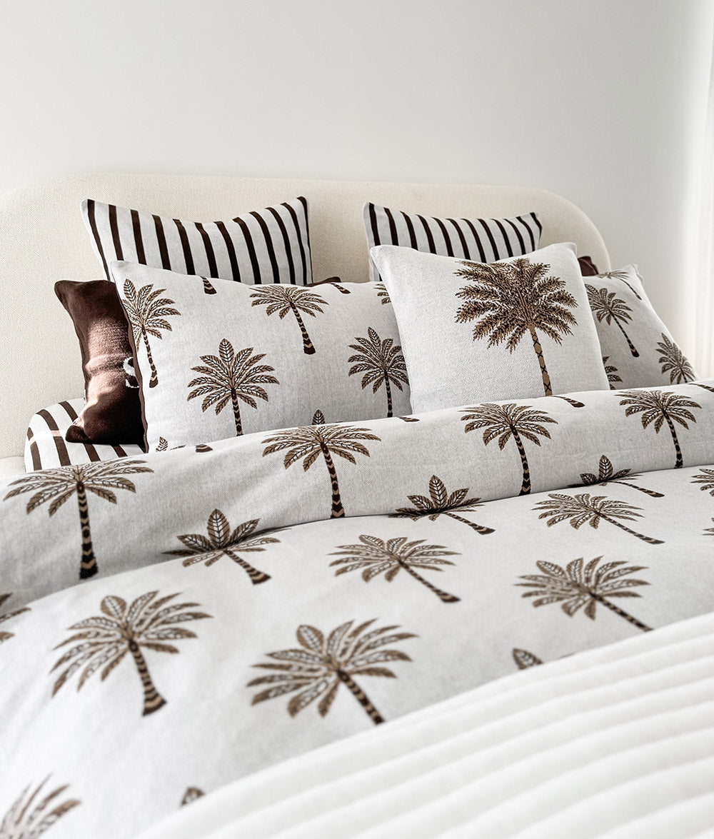 Striped euro pillowcases layered behind palm print cushions on a bed with palm print bedding