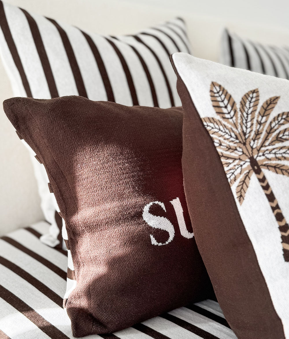 Chocolate lumbar cushion in front of a striped euro pillowcase and a palm print cushion