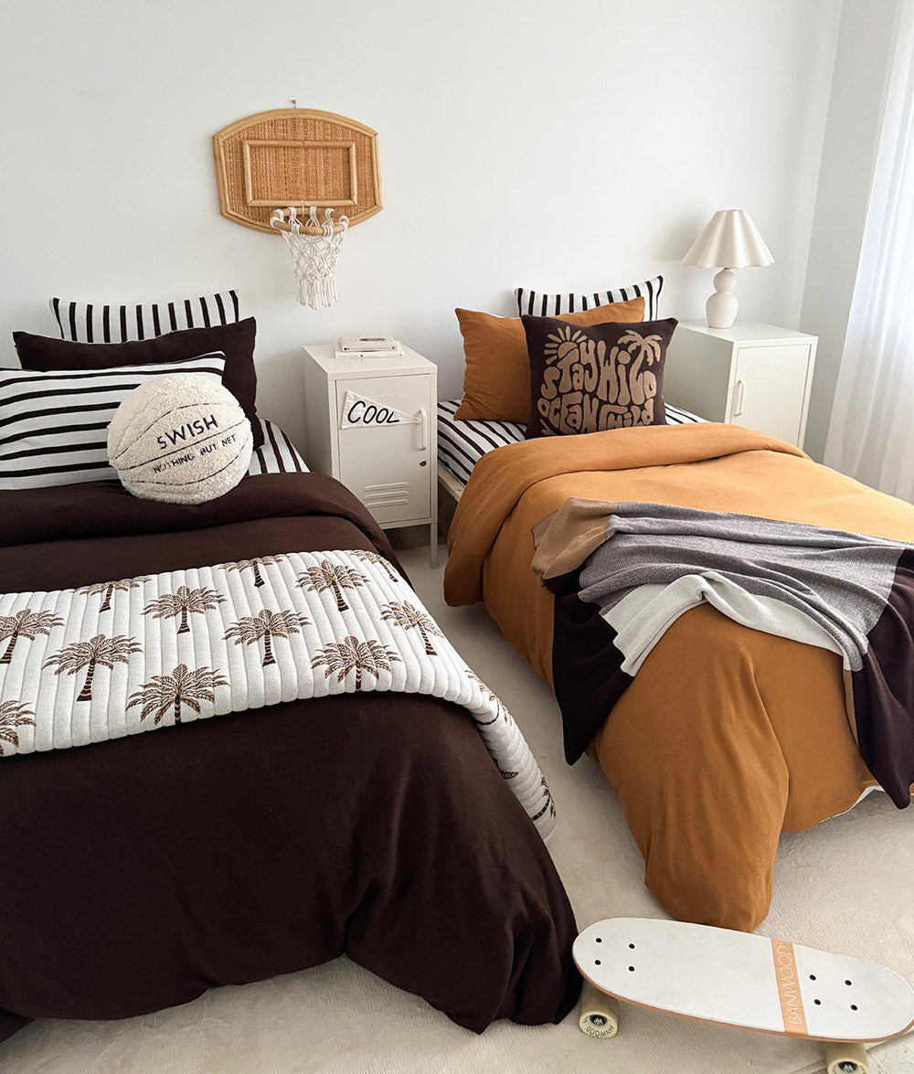 Two kids beds in chocolate and tobacco bedding with the basketball sherpa cushion at the head