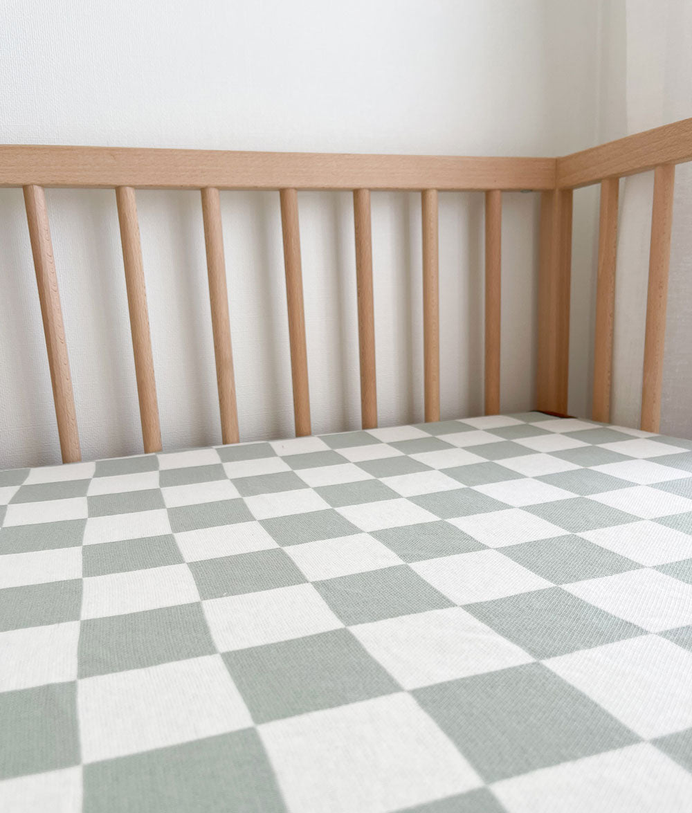 Sage Gingham jersey cotton cot sheet in a timber cot, showing the sage and ivory check