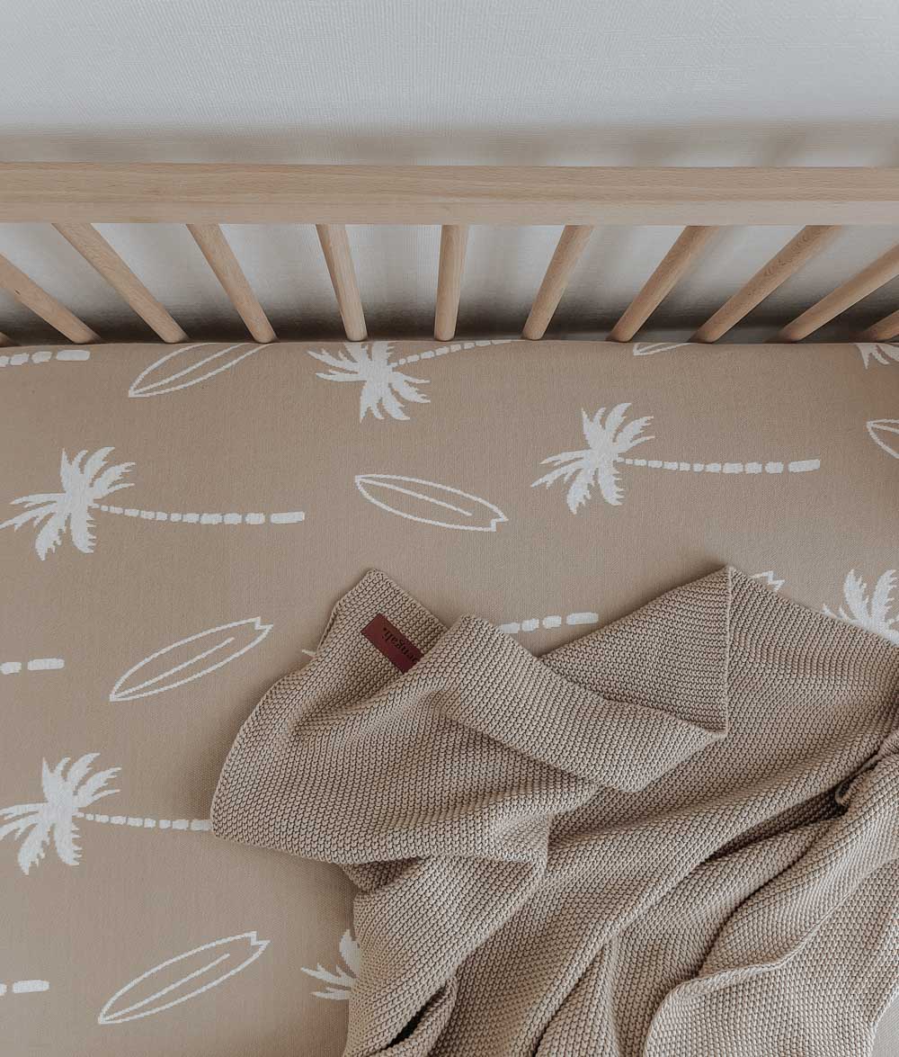 Sand Surfing Palm jersey cot sheet in a timber cot with a soft knitted blanket