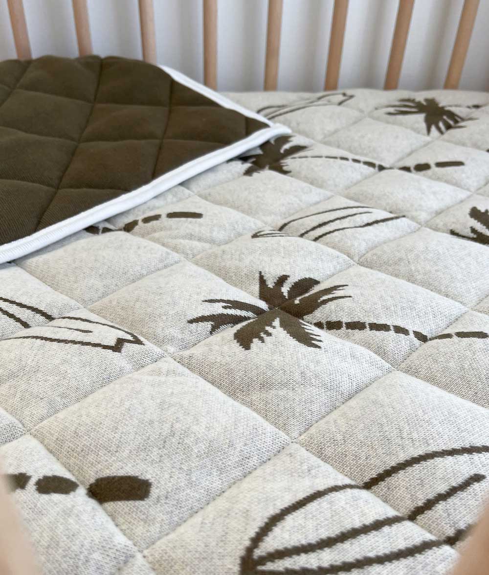 Olive Surfing Palm reversible kids quilt with its plain olive reverse folded back in a timber cot