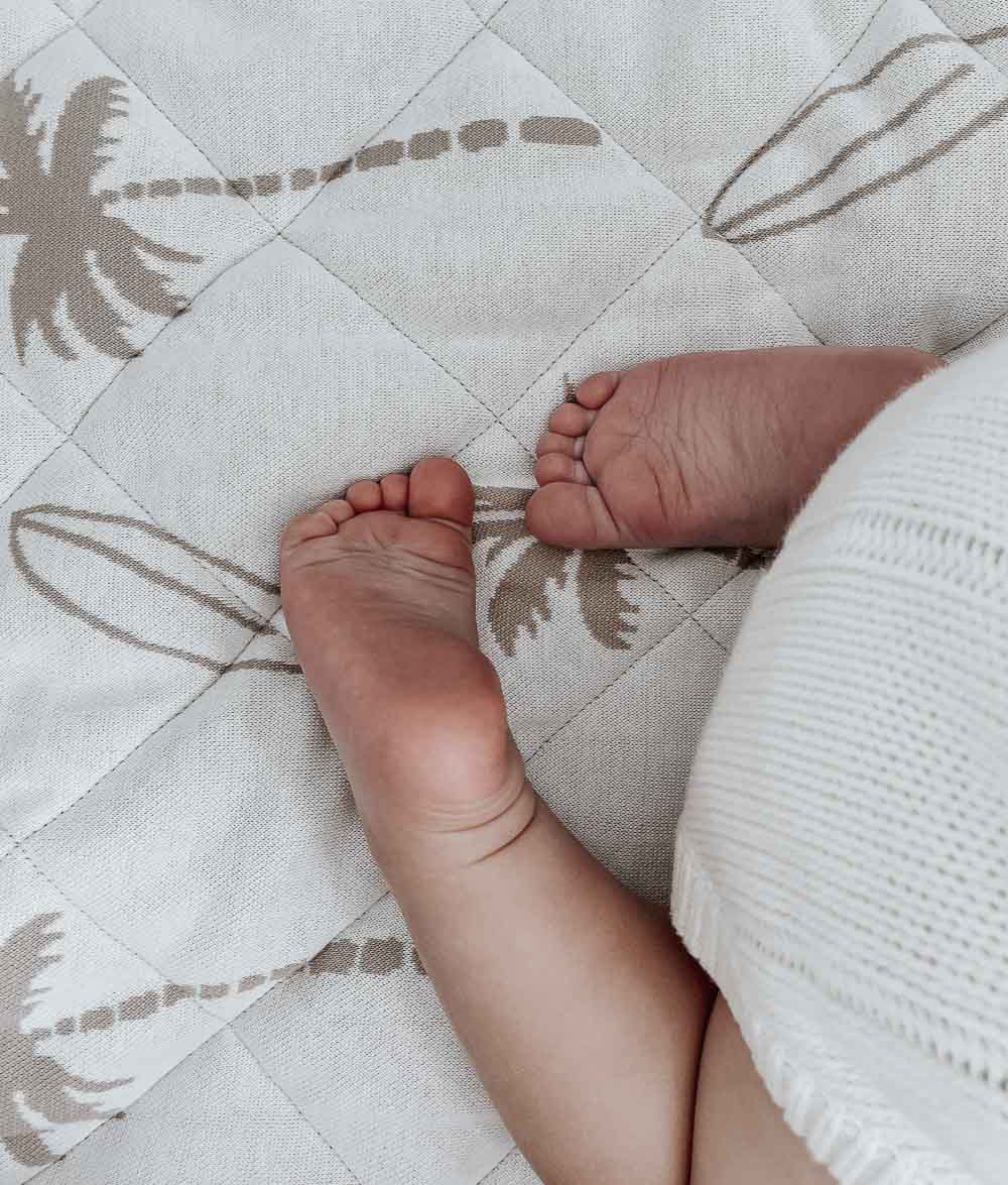 Baby's feet on a natural Surfing Palm reversible cotton quilt with sand palm and surfboard print