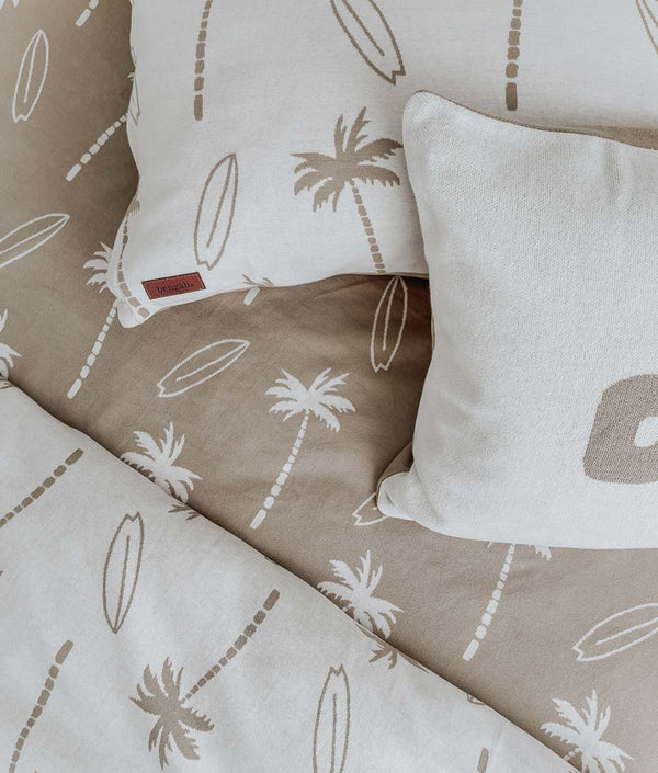 Surfing Palm kids pillowcase with leather label beside a DUDE pillowcase on a sand Surfing Palm fitted sheet