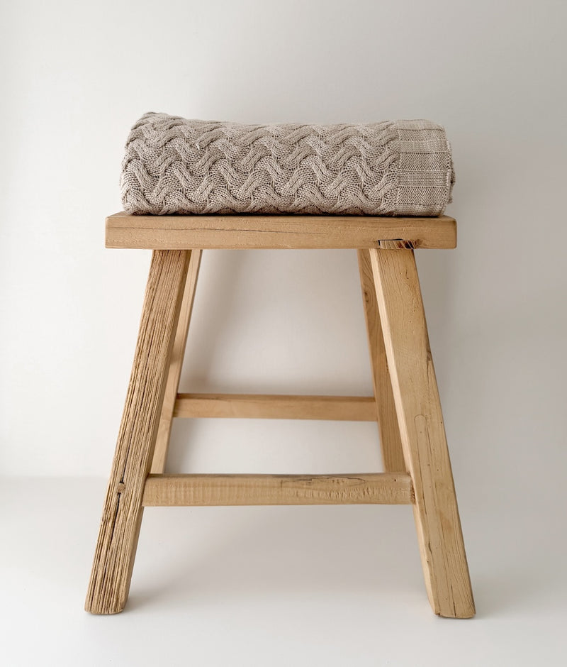 Greige Wave throw folded on a timber stool against a white wall
