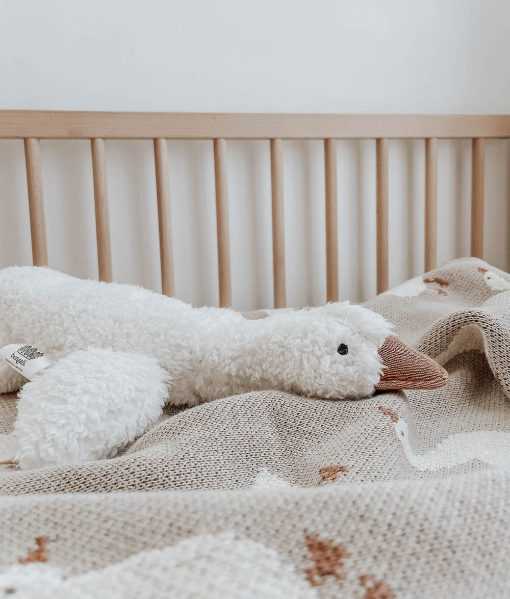 Sherpa goose comforter with a tan beak lying across a cot beside timber rails
