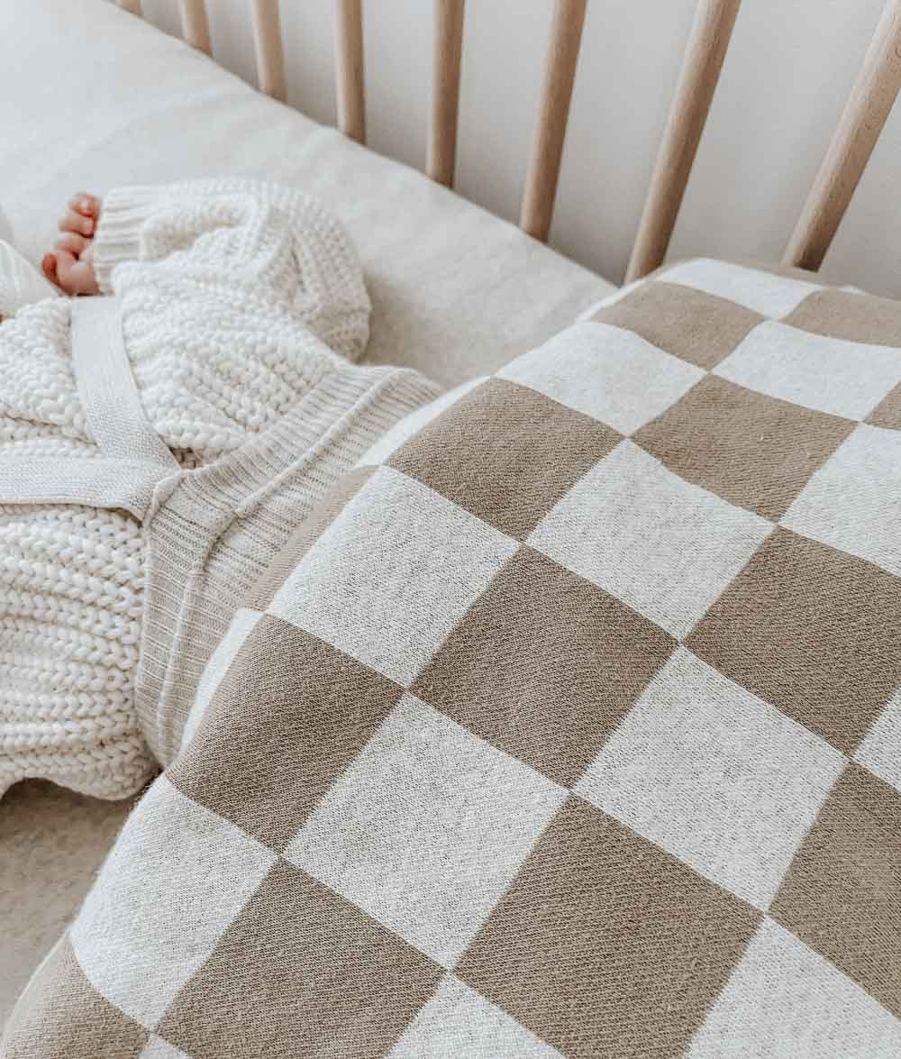 Close-up of a baby in a cream knit tucked under a khaki gingham jersey cotton cot duvet cover