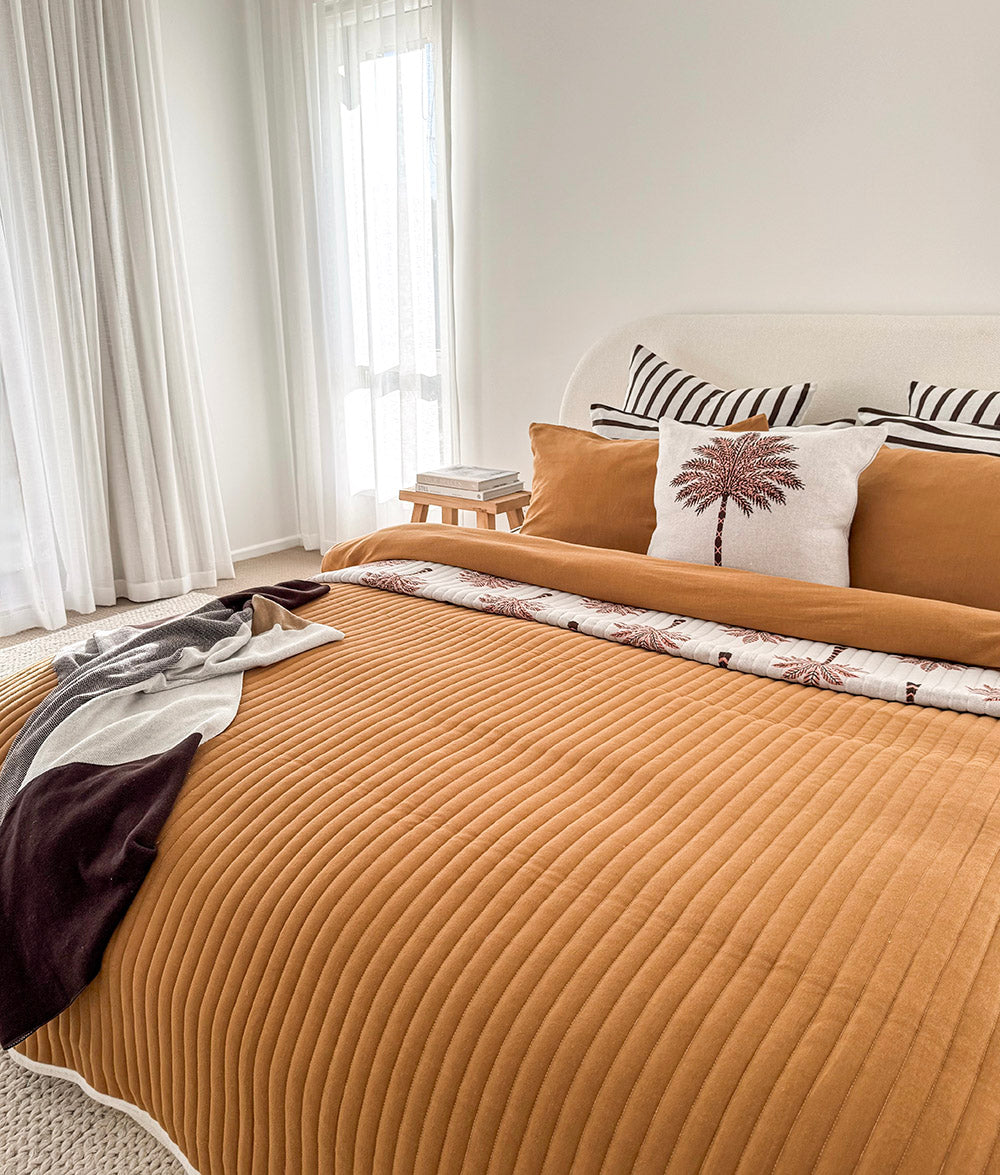 Bedroom with a tobacco quilted bed and chocolate and ivory striped pillows at the head