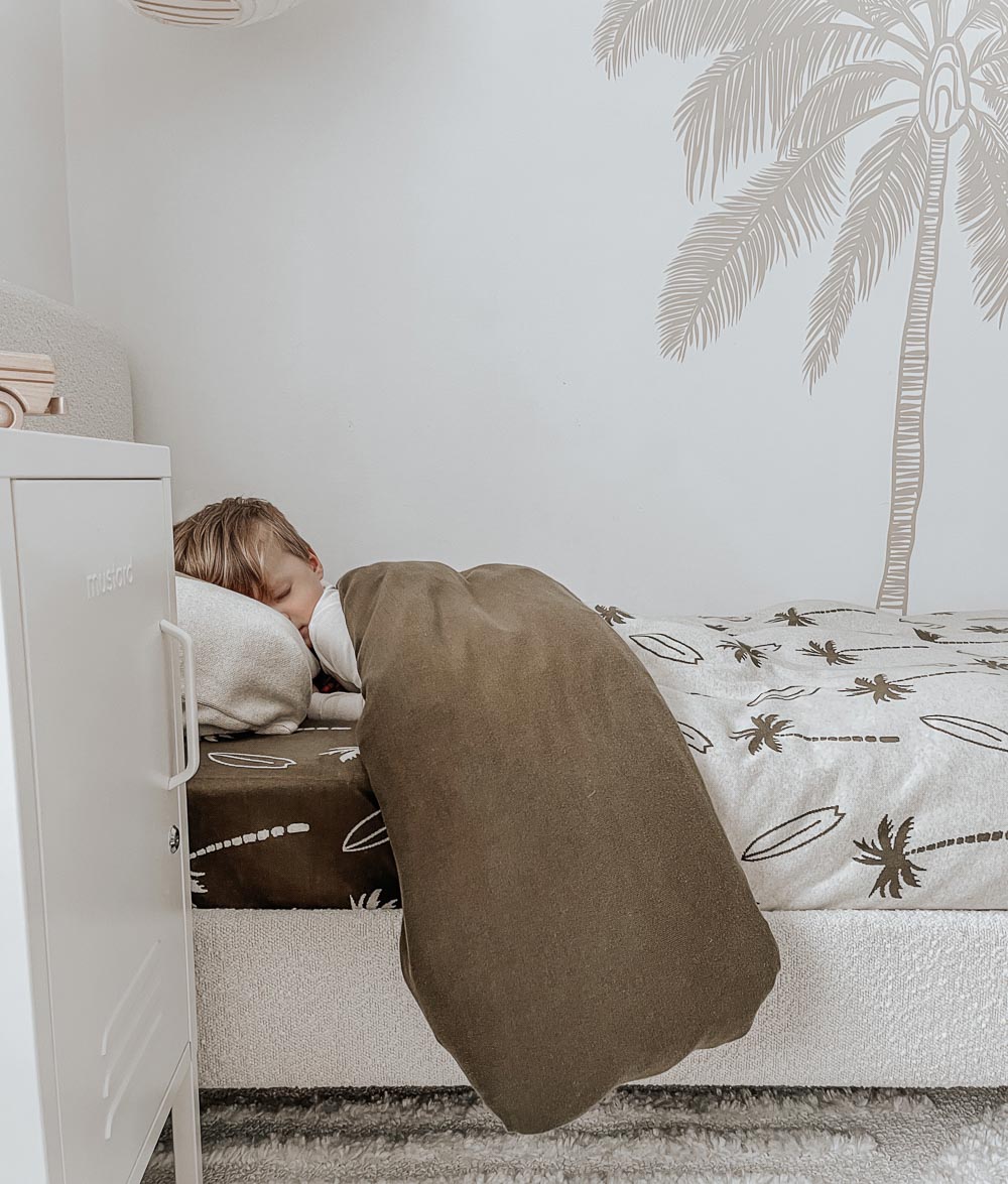 Child asleep under an olive knit blanket on a bed dressed with a Surfing Palm kids duvet cover and olive sheet