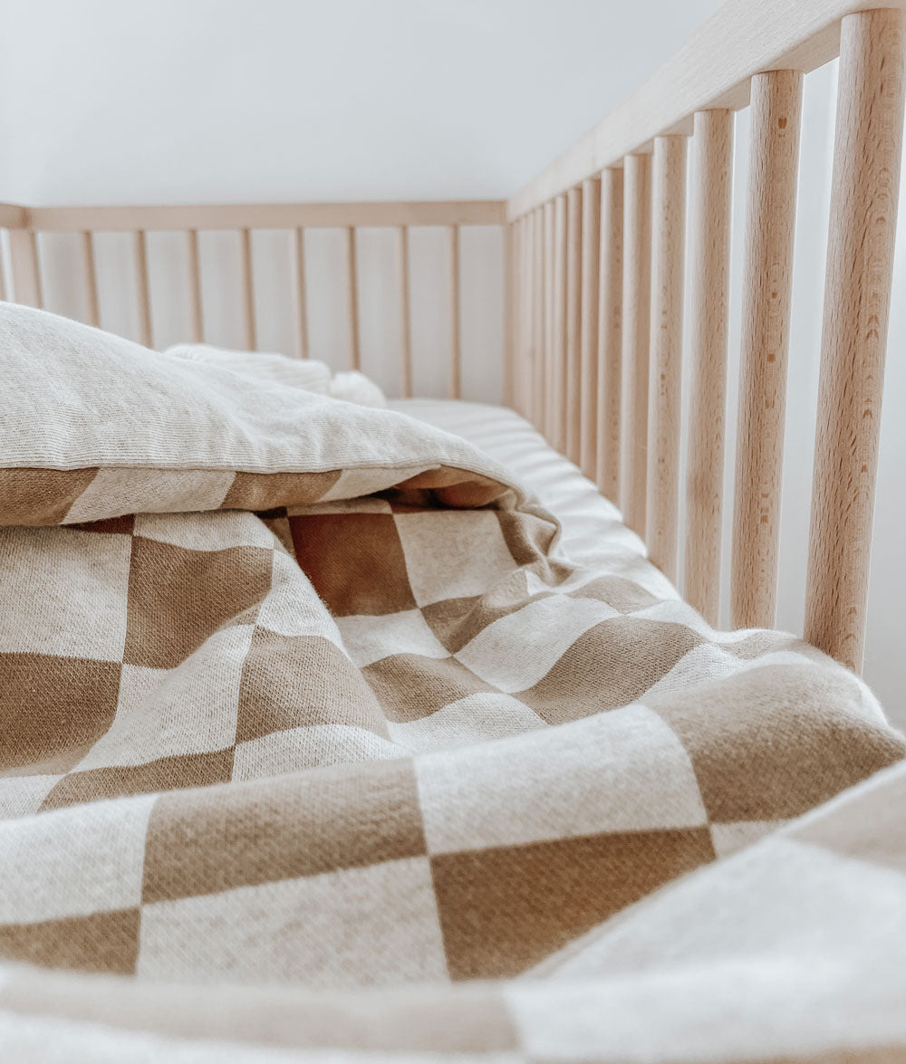 Khaki gingham jersey duvet cover folded back in a timber cot over a natural marle sheet