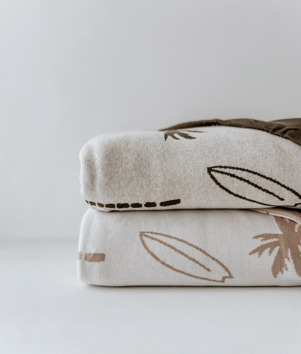Two folded Surfing Palm duvet covers stacked, showing the natural and olive palm and surfboard prints