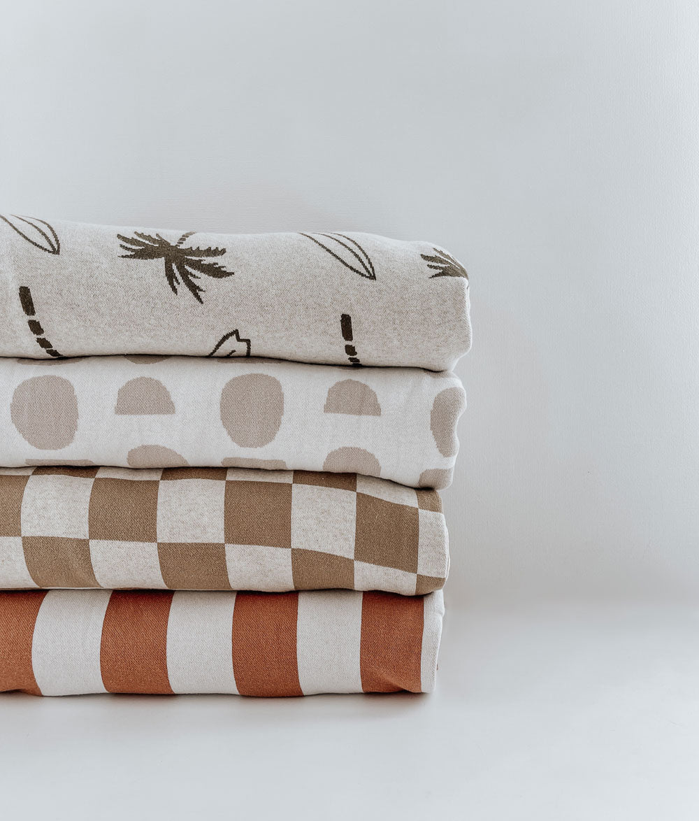 Khaki gingham jersey duvet cover folded in a stack with Surfing Palm, spot and rust stripe covers