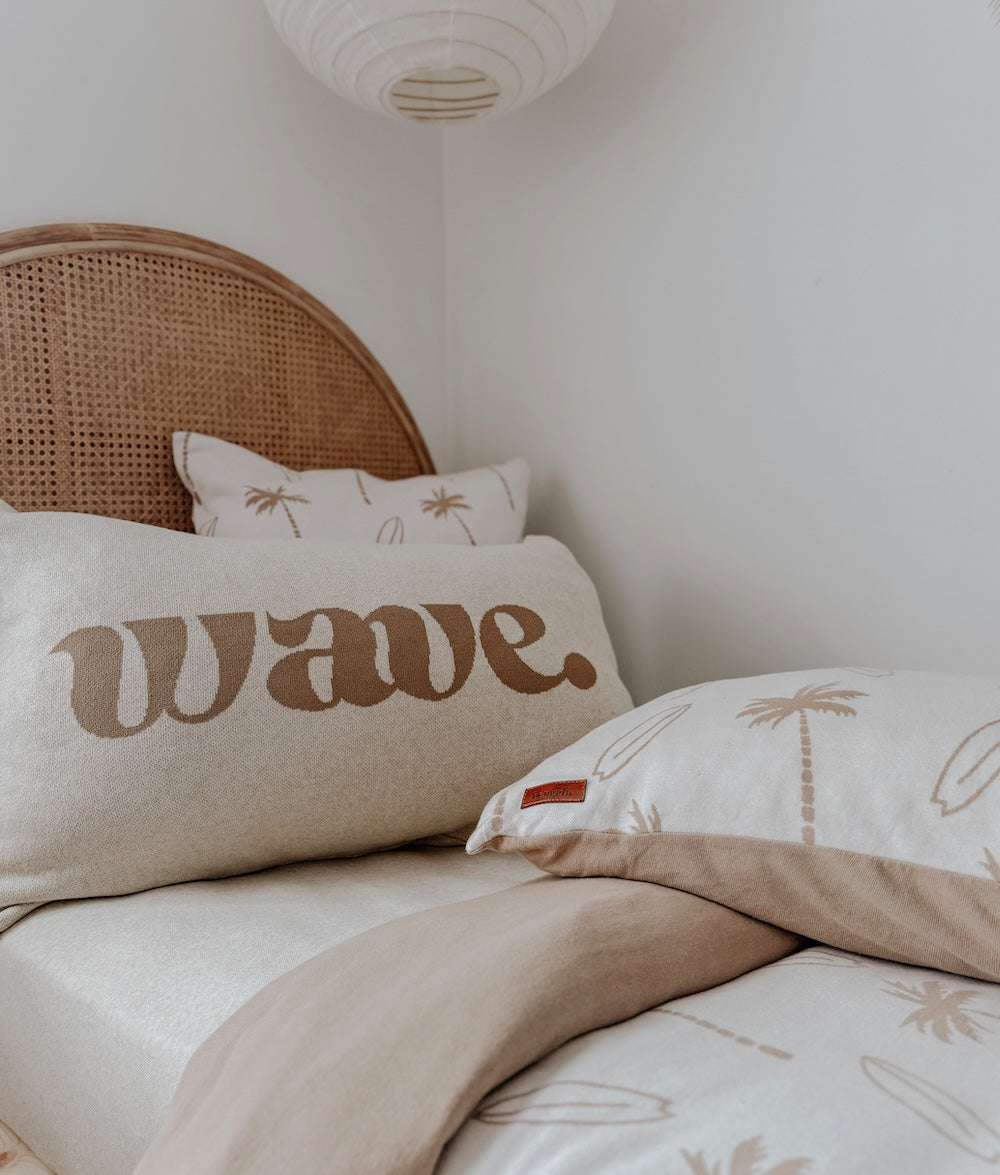 Wave lettering cushion in front of the palm print euro pillowcase on a rattan bed