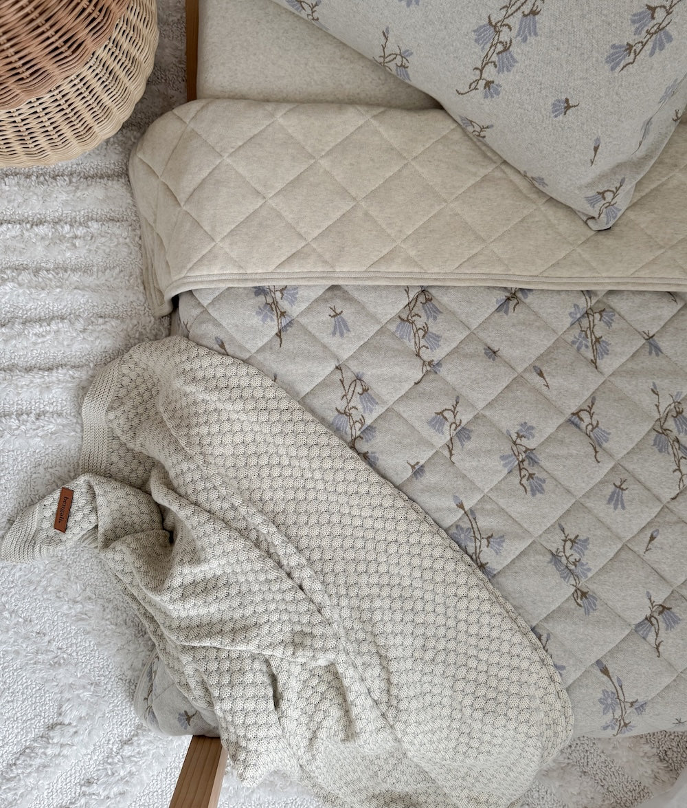Corner of the pebble knit blanket on a diamond quilted floral cot quilt