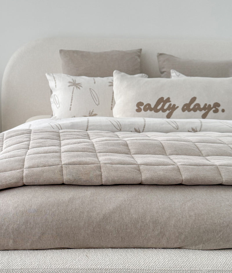 Salty Days cotton pillowcase with palm print pillowcases and a quilted greige coverlet on a boucle bed