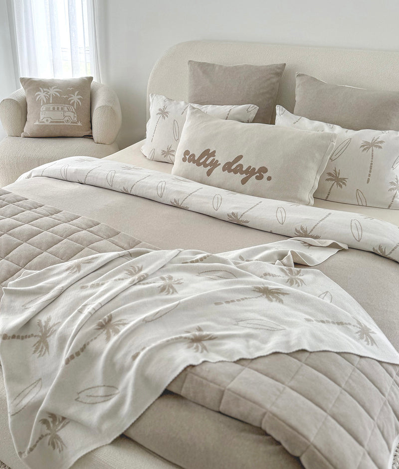 Queen bed styled with a Salty Days pillowcase, palm print bedding and a quilted greige throw