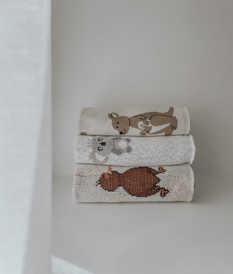 Stack of folded knitted cotton baby blankets, the Kangaroo design on top of koala and rust designs