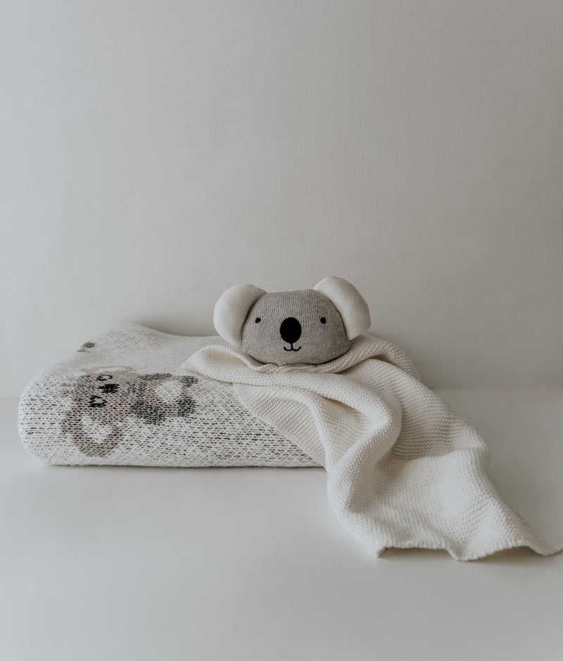 Koala baby comforter snuggly with its cuddle cloth draped over a folded koala knit blanket