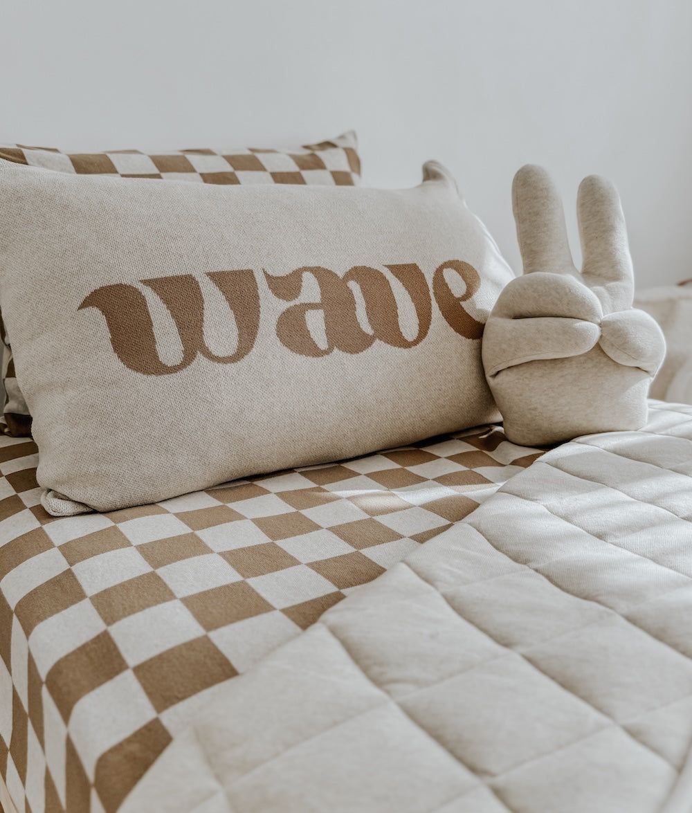 Wave lettering cushion and a bunny sherpa cushion on a bed with khaki gingham bedding