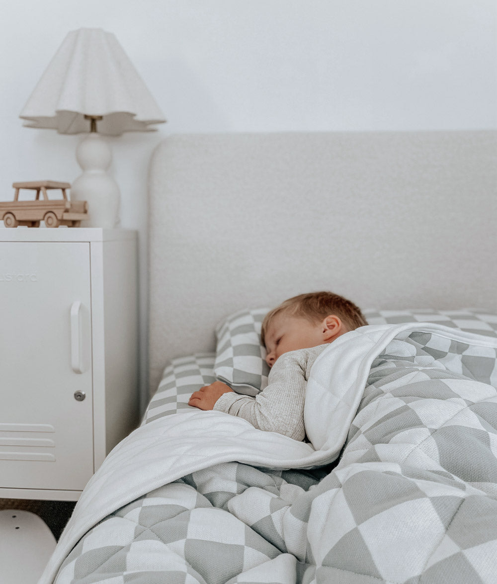Toddler asleep in a boucle bed under a Sage Gingham reversible quilt with its ivory side turned down