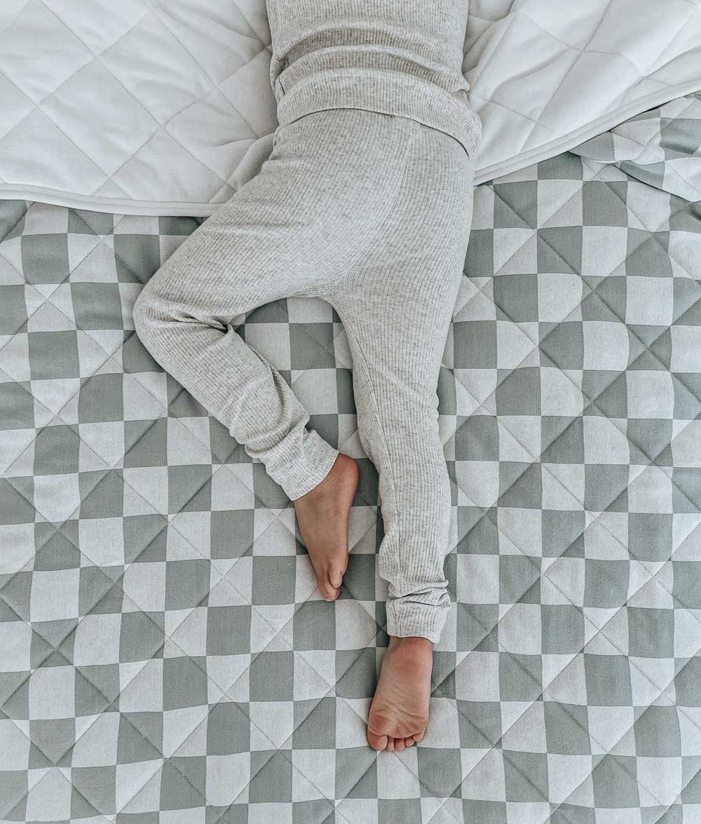 Overhead view of a child's legs on a quilted Sage Gingham reversible cotton quilt