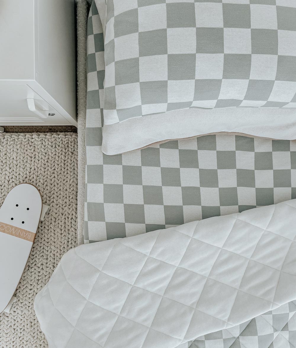 Close-up of a Sage Gingham fitted sheet and matching pillowcase with a white quilt and skateboard