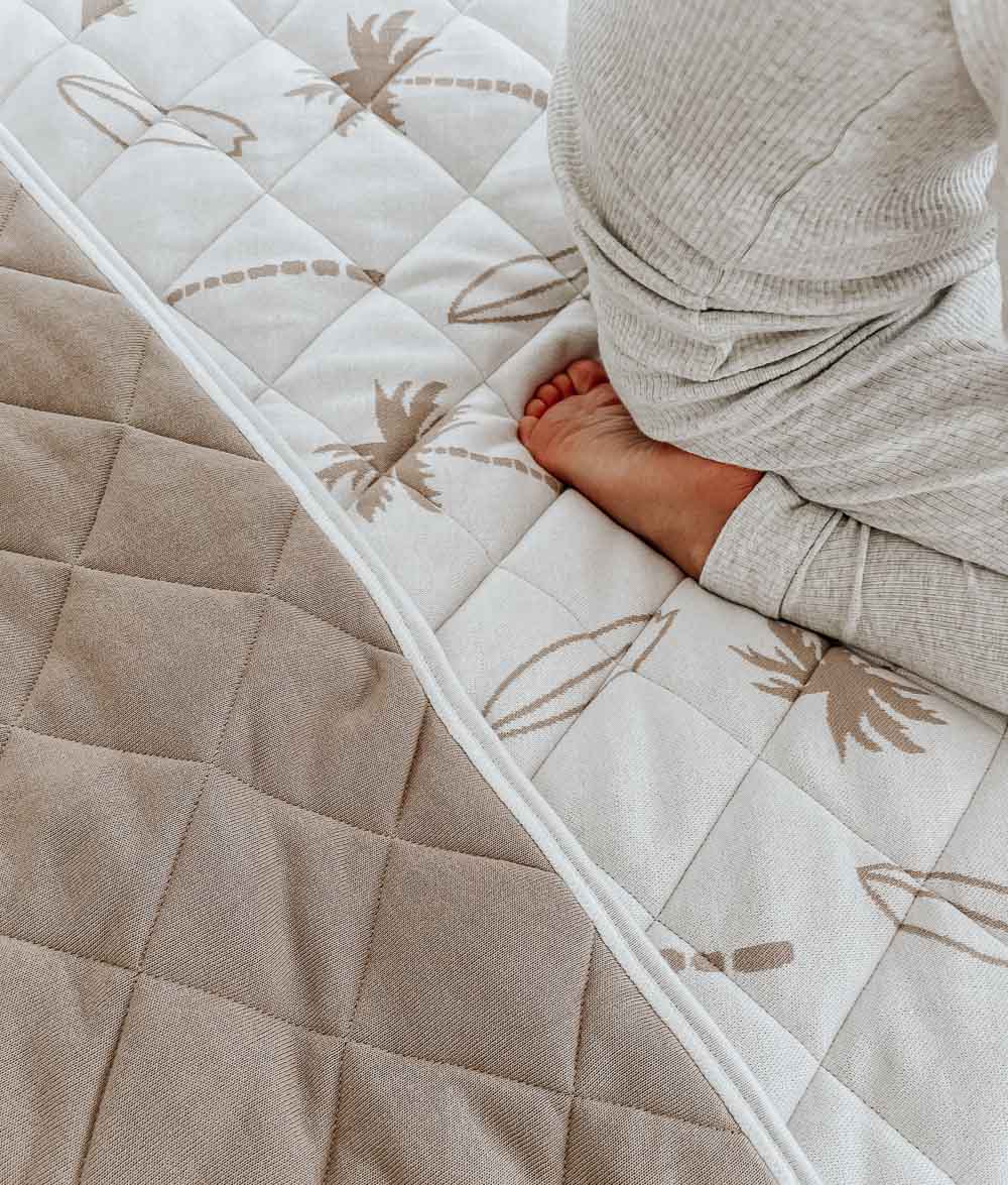 Child's foot on a Surfing Palm reversible quilt, the edge turned to show its plain sand quilted reverse
