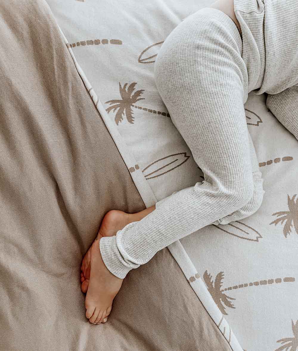 Close-up of a child's bare feet on a natural Surfing Palm jersey duvet cover with palm and surfboard print