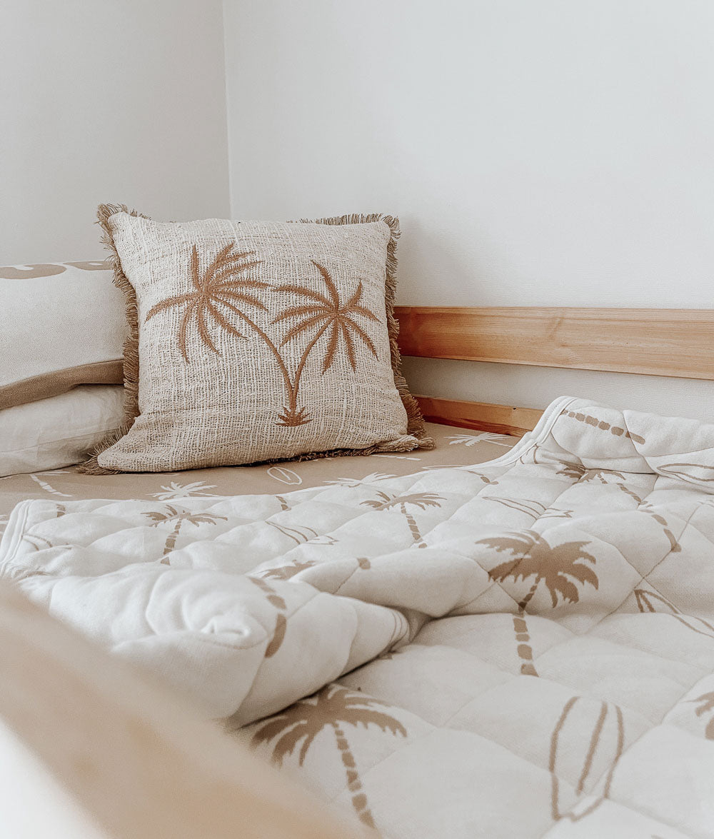 Kids bed with a Surfing Palm quilt over a sand Surfing Palm fitted sheet and a fringed palm tree cushion
