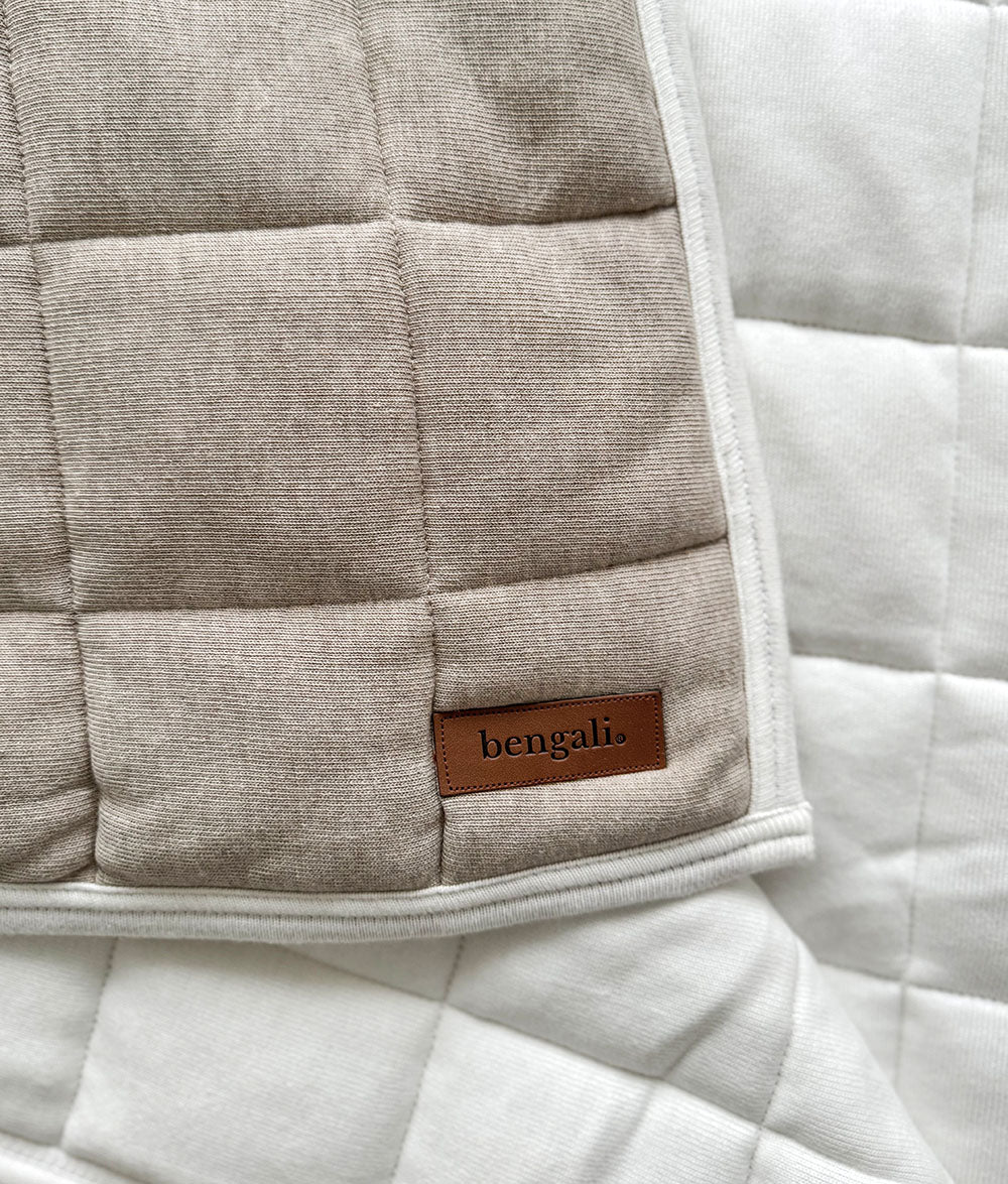 Corner of the dune quilt turned back to show the plain ivory reverse and leather Bengali tab
