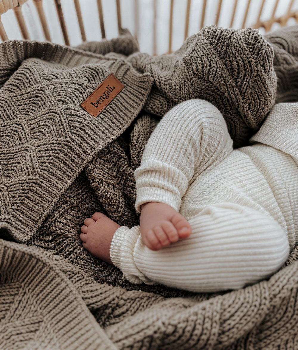 Close-up of the stone shell stitch texture with a baby in cream knitwear resting on it